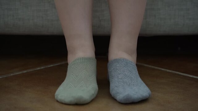 Close-up of woman's hands putting on mismatched socks of different color on her feet. Woman wearing different colored socks. Uniqueness, difference and independence concept. Front view