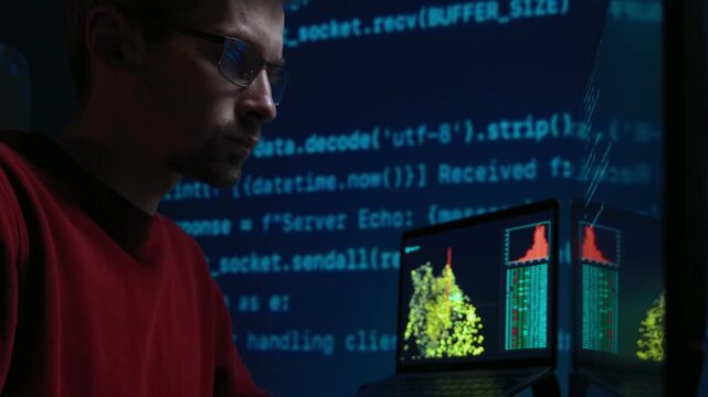 Focused data scientist writing code on keyboard in a dimly lit workspace in front of multiple monitors, with running programming script lines casting a blue glow across the dark office. 