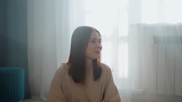 Woman tutor coaching grammar at home, seated by sunlit window wearing cozy sweater, speaking softly with thoughtful expressions, indoor study setting with sheer curtains and radiator, calm reflective