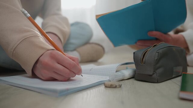 Close up hand writing on workbook mentor reviews notes from blue journal tutor offers verbal correction while student practices pencil case and eraser in foreground bright ambient light collaborative