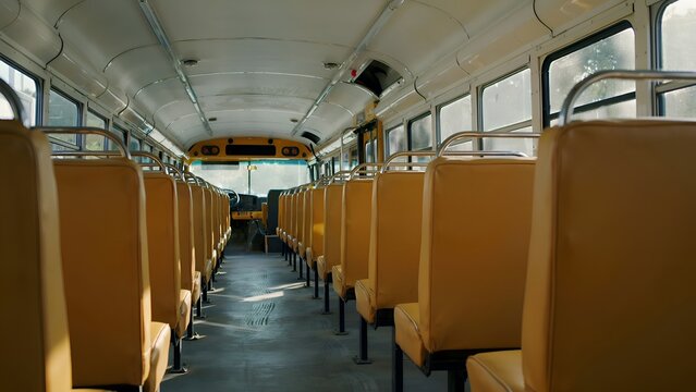 Empty school bus interior features rows of yellow vinyl seats and overhead lighting