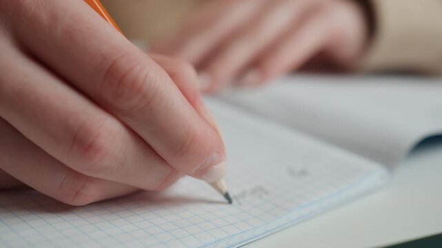 Closeup caucasian female student writing grammar exercises on grid paper, pencil moving across pages, neat handwriting, tutor guidance implied, warm ambient light, quiet home study desk atmosphere