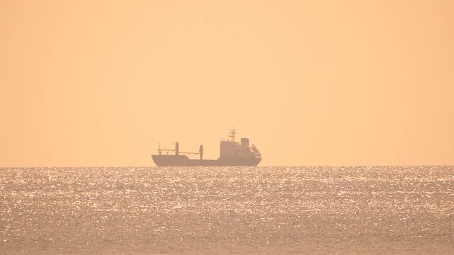 Cargo ship ocean sunset a large freight vessel sails across the shimmering ocean during a hazy golden hour