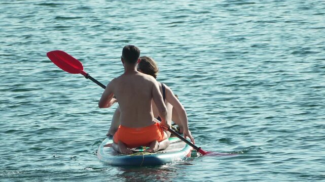 Paddleboarding couple summer paddling together on calm blue water, enjoying a relaxing water sports activity