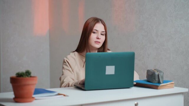 Caucasian woman working on laptop desk, warm sunset glow on wall, potted plant and camera bag on table, focused editing and planning, content strategy session, compact studio corner, modern remote