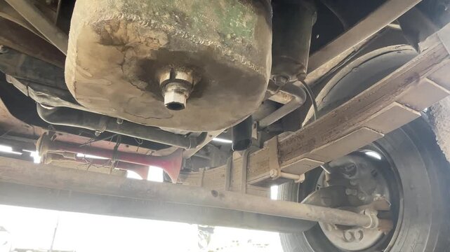 commercial truck circular metal cover under body during carwash process showing undercarriage chassis of heavy duty vehicle for cleaning maintenance inspection outdoor station.