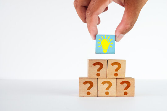 Hand placing a blue wooden block with a yellow lightbulb icon on top of stacked blocks with question marks. Concept of problem solving, creative ideas, finding solutions, and business innovation.