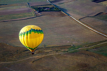 High angle aerial view of yellow hot air balloon flying over agricultural fields in Segovia. © Margarita