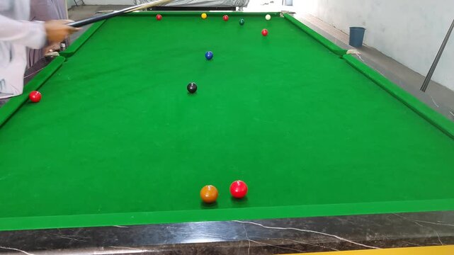 Professional snooker player aiming cue on green felt table, billiards match with colorful balls, indoor sports recreation and hobby