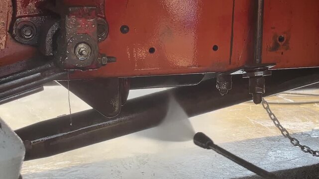 commercial truck red underbody frame water spray during carwash process showing undercarriage chassis of heavy duty vehicle for cleaning maintenance inspection outdoor station.