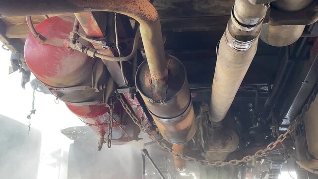 commercial truck exhaust pipes dual pressure wash during carwash process showing undercarriage chassis of heavy duty vehicle for cleaning maintenance inspection outdoor station.