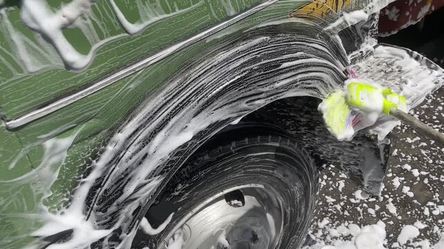 commercial truck wheel arch fender foam water during carwash process showing undercarriage chassis of heavy duty vehicle for cleaning maintenance inspection outdoor station.
