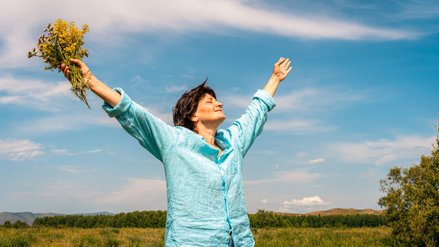 Woman standing in green field with her arms outstretched, facing sun, embracing happiness and beauty of nature. Women's mental health, accepting one's age