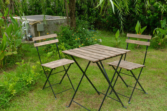 Wooden table and chair set in garden on a sunny day,outdoor seating for restaurant or cafe,Neat paved patio with sitting area and small garden in forest.