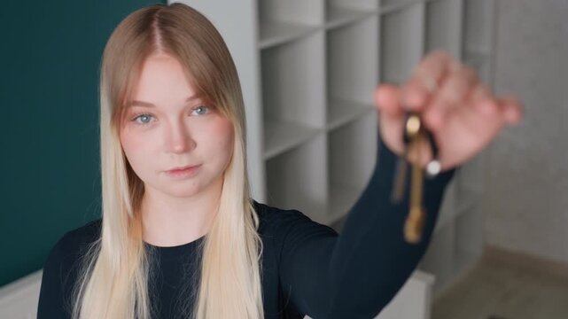 White woman leasing agent presenting apartment keys, poised portrait in minimalist corridor, focused closeup of hand and keychain, neutral expression for rental handover and listing presentation, move