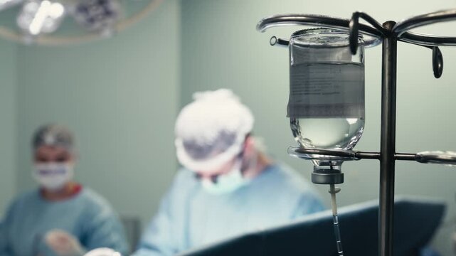 Bottle of clear IV solution attached to an infusion pole in an operating room. Concept intravenous therapy, sterile care, medical equipment and patient safety.