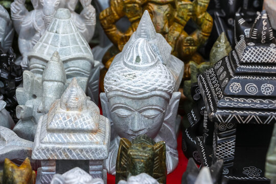 Assorted handmade stone carved Buddha head sculptures, miniature temples and Ganesha figurines on display at a market in Hampi, India. Traditional Hindu and Buddhist art souvenirs.