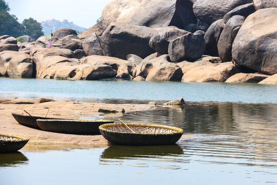 Traditional round wicker coracle boats moored on the rocky bank of the Tungabhadra River against giant granite boulders in Hampi, India. Scenic landscape view, historic travel destination.