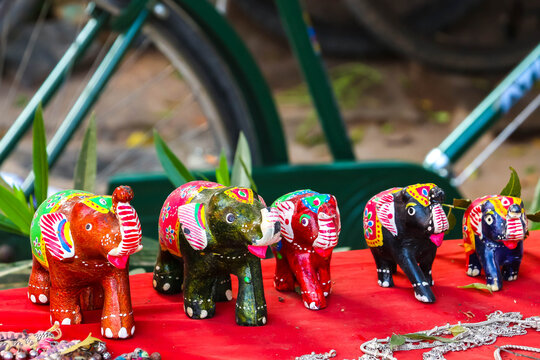 Line-up of colorful handmade wooden painted elephant figurines and toys on display on a market stall in Hampi, India. Traditional ethnic souvenir crafts collection, folk art and decor.