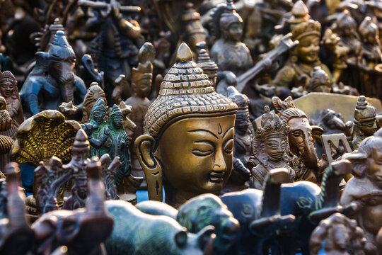 Assorted antique brass and metal Hindu god figurines, Buddha head and animal statues on display at a market in Hampi, India. Traditional religious artifacts, spiritual art objects and souvenirs.