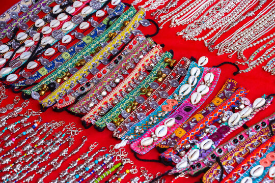 Assorted colorful handmade Indian bracelets and anklets decorated with cowrie shells, bells and embroidery on display at a market in Hampi, India. Traditional ethnic fashion accessories collection.