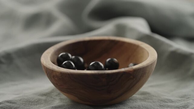 Slow motion ripe blackcurrant falling in wood bowl