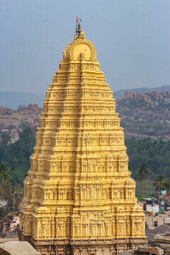 Main gopuram tower of Virupaksha Temple against landscape and boulder hills in Hampi, India. Historic Hindu temple architecture, sacred pilgrimage site, cultural heritage landmark, tourist attraction.