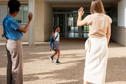 Schoolgirl waving goodbye to parents while entering elementary school building