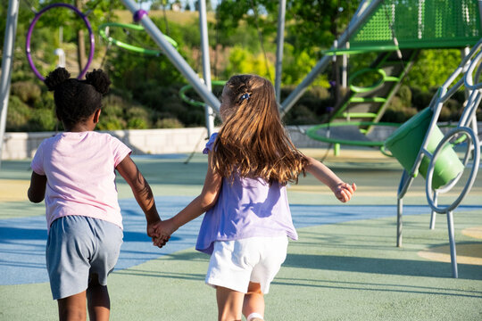 Diverse children holding hands, running towards a playground structure on a sunny day