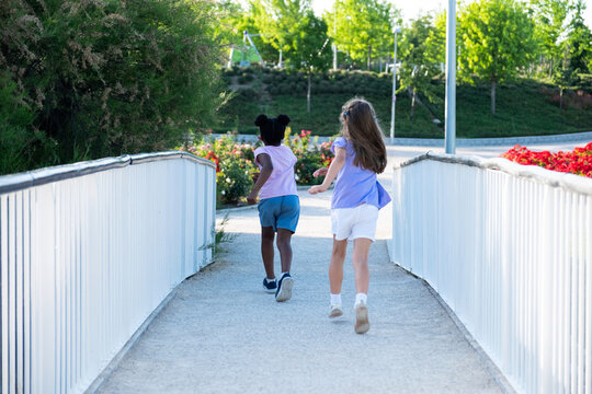 Two young diverse girls running and playing together on a bridge in an outdoor park
