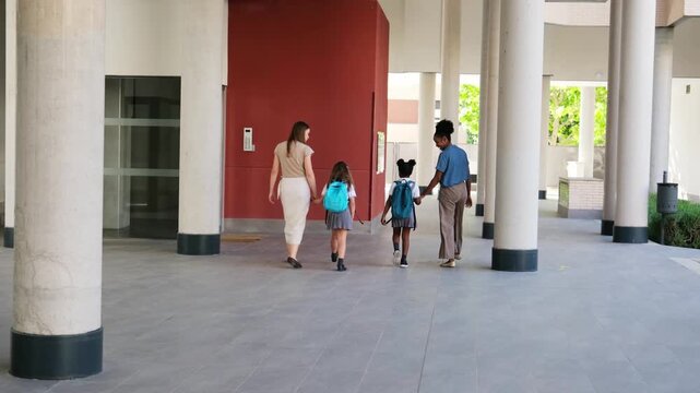 Multiracial female couple walking their children to school in a modern building hallway