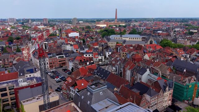 Aerial view video clip of Ghent city rooftops, tall red construction crane, historic brick buildings, industrial chimney, and urban cityscape in East Flanders, Belgium