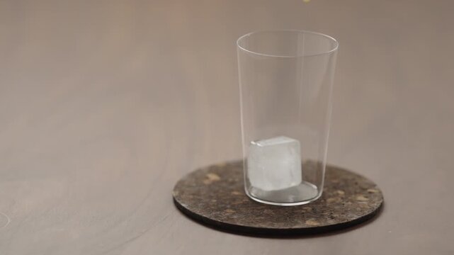 Slow motion pour orange juice in a glass with ice cube on a wood table
