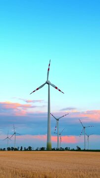 Wind turbines in a field during sunset. Wind turbines turn slowly in a field as the sun sets. The sky shows colors of blue and orange.
