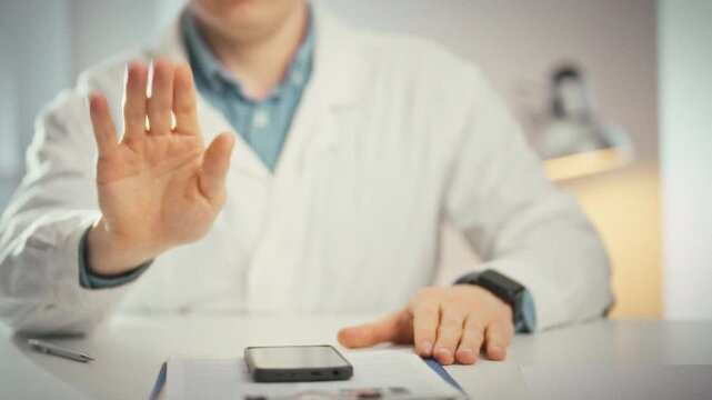 A doctor in a white coat extends a hand, palm outward, signaling stop in a close-up gesture. This universal medicine concept conveys a clear warning or refusal in a clinical office setting