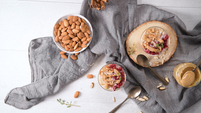 Overhead view of healthy breakfast bowls with raspberries, nut butter, and almonds on a grey linen cloth