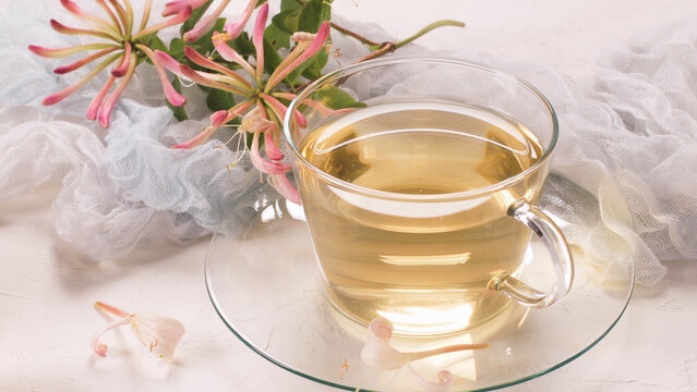 Glass cup of herbal honeysuckle tea with fresh blossoms on a light textured surface