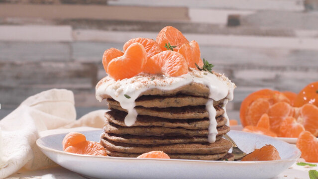 Stack of fluffy pancakes with yogurt cream and fresh mandarin oranges on a plate