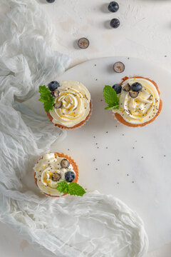 Overhead view of cupcakes with white frosting and fresh blueberries on a marble board