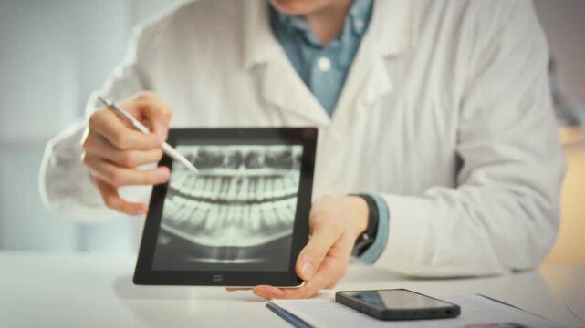 A tablet displaying a panoramic dental image sits in a dental office as a doctor in a white coat guides the patient through a consultation, highlighting problem teeth and outlining the treatment plan