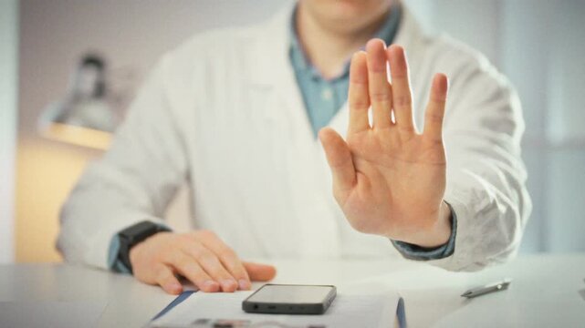 Displaying a stop gesture, a doctor in a white coat stands in his office, hand raised to signal halt. This medicine-themed image highlights clinical authority and clear communication in healthcare