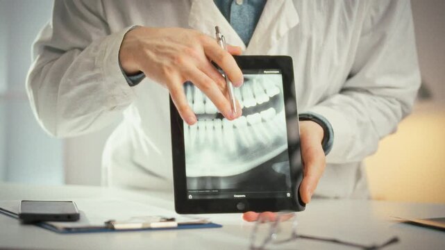 Doctor in crisp white coat examines patient in bright dental office, using a tablet to display a panoramic image of all teeth during a consultation, highlighting issues and outlining a treatment plan