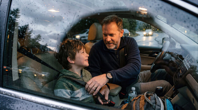 Father helping son buckle up seat belt in car on a rainy day