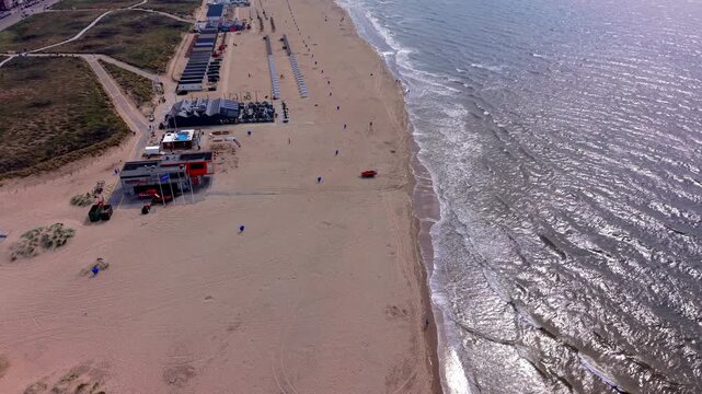 Aerial view video clip of Katwijk aan Zee sandy beach, lifeguard station, rescue boat, beach pavilions, glistening North Sea waves, and coastal dunes in South Holland, Netherlands