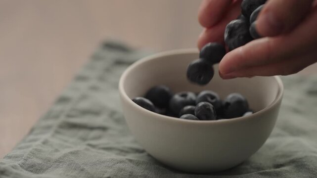 Slow motion man hand put blueberries to a ceramic bowl