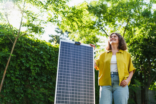 Woman standing in a green park holding a solar panel in the sunlight