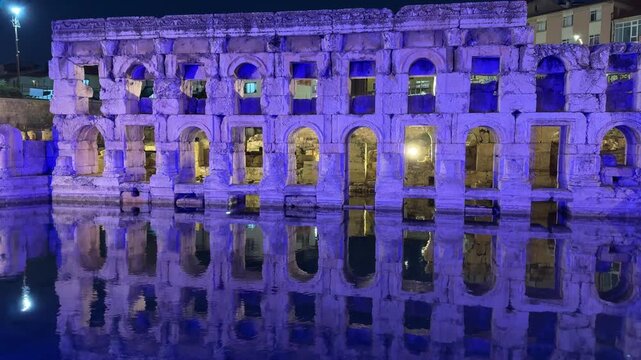 Illuminated Ancient Stone Aqueduct Ruins at Night with Water Reflection. Basilica Therma is an ancient Roman spa town located in the Yozgat province. 4k video