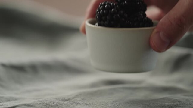 Slow motion man hand put fresh ripe blackberry in a white small bowl
