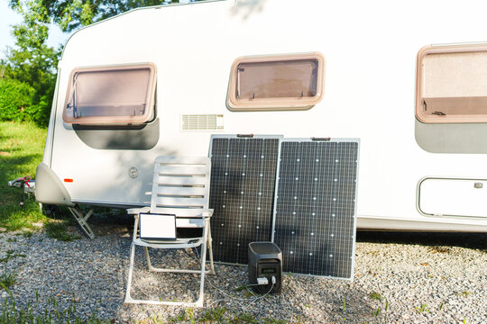 Portable power station with solar panel charging gadgets near a travel trailer caravan