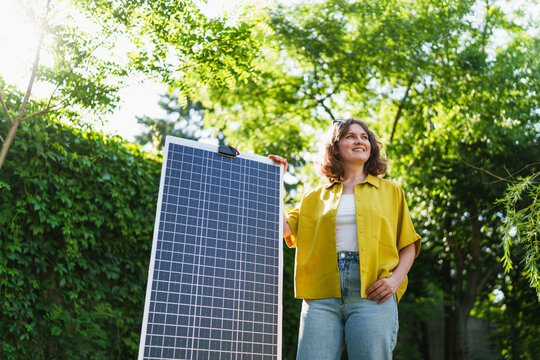 Woman standing in a green park holding a solar panel in the sunlight